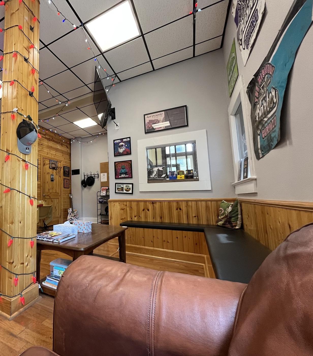 The waiting side: a leather sofa, a wooden bench, a pillar wrapped in red string lights, and a hand painted sign reading The Missouri Barber Company.